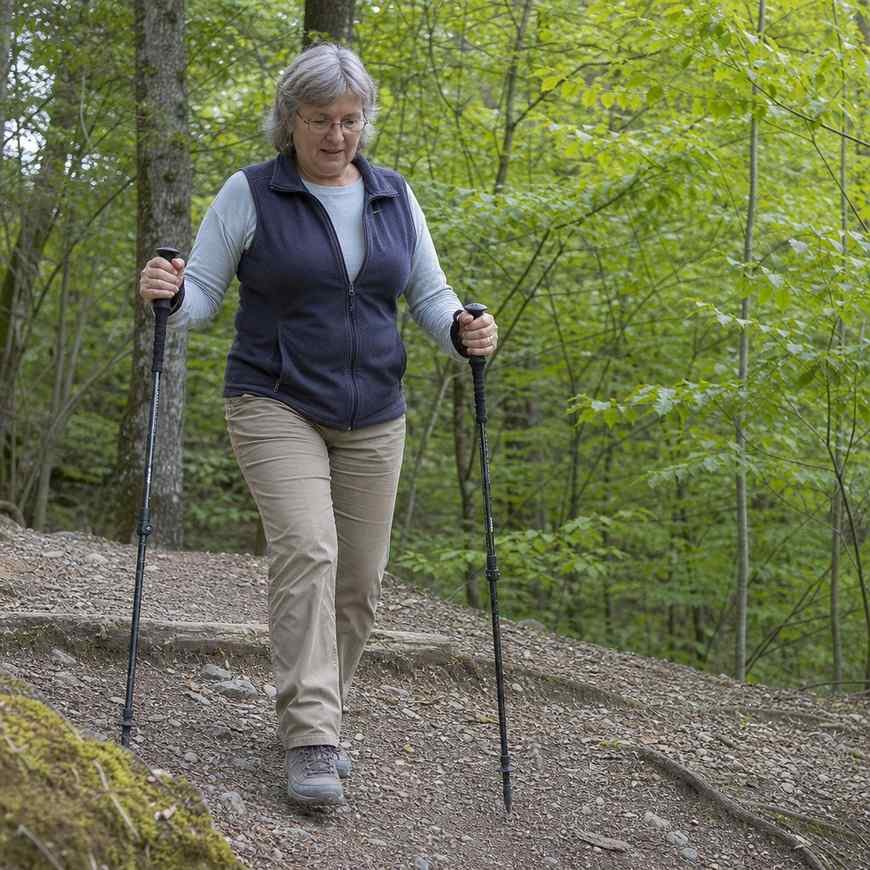 An older woman using a pair of walking poles on a gentle gravel trail in daylight