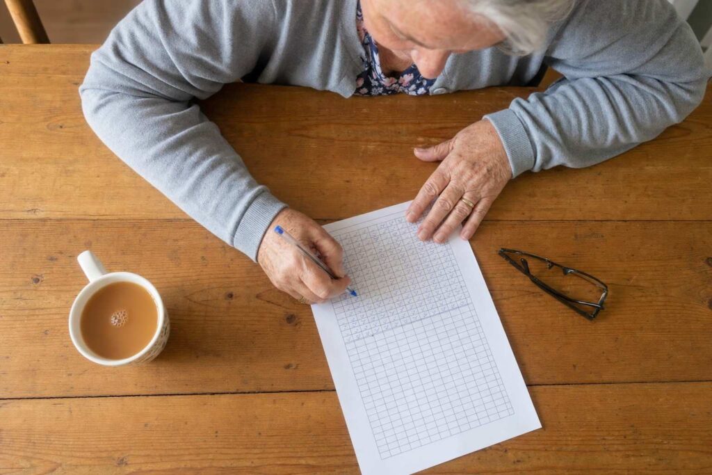 Overhead close view of an older person's hands filling in a printed walking tracker sheet on a kitchen table