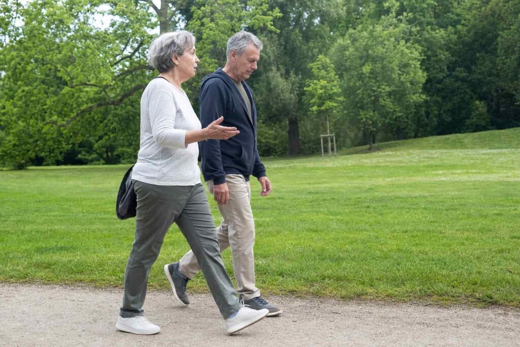 Two older friends walking at an easy pace on a flat grassy park path, seen from the side