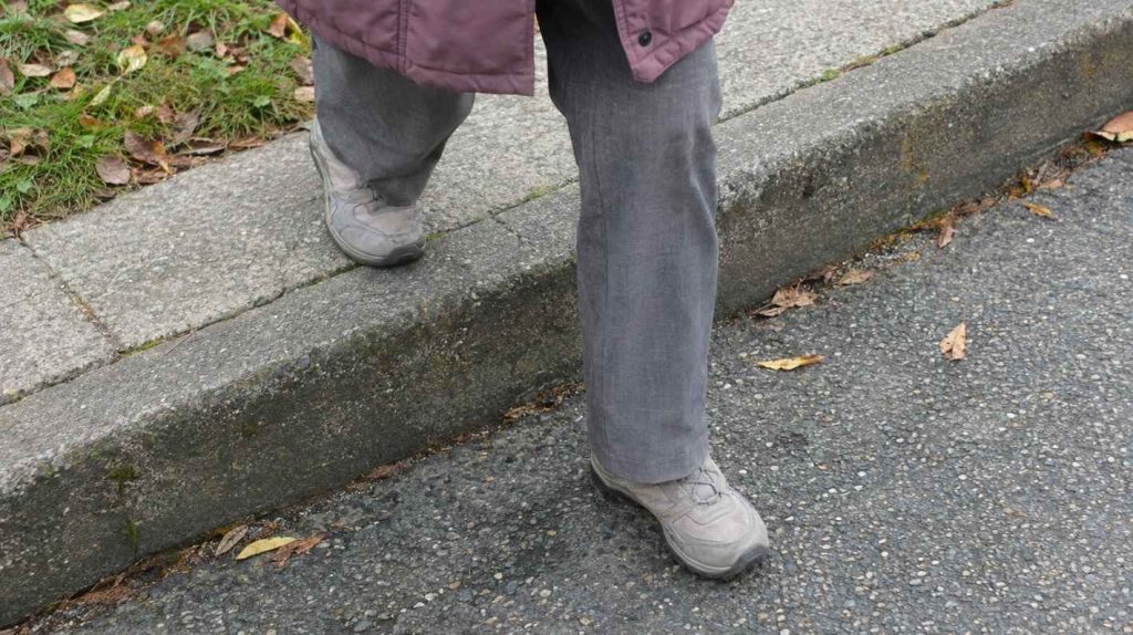 Seen from above, an older walker's feet stepping carefully down from a sidewalk curb